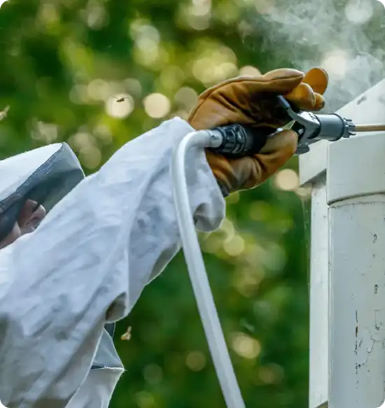 Worker in protective suit and glove using a pressure washer to clean an outdoor utility box.